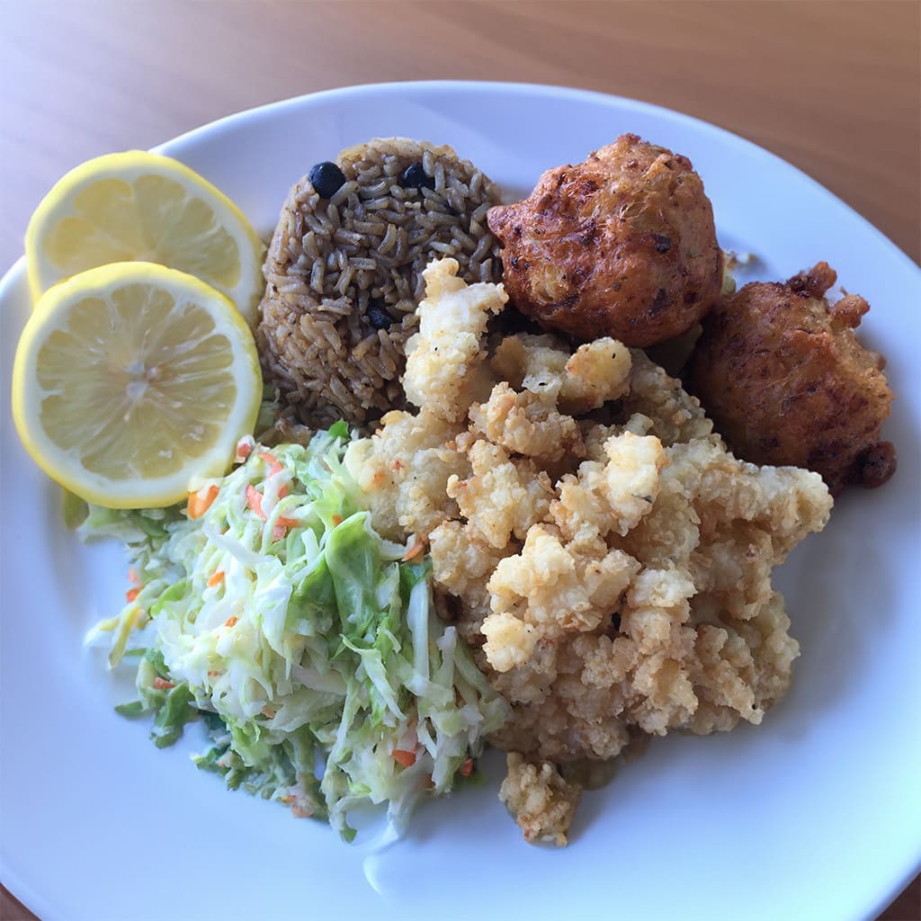A plate of golden, crispy Cracked Conch, nestled beside a mound of flavorful Rice and Peas