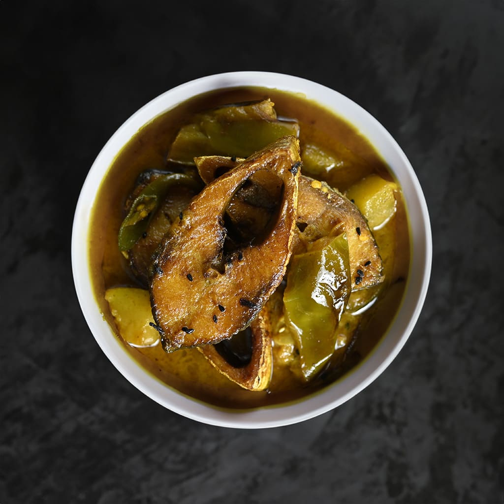 A steaming plate of golden Hilsa Curry, the fish's delicate flesh shimmering in mustard gravy.