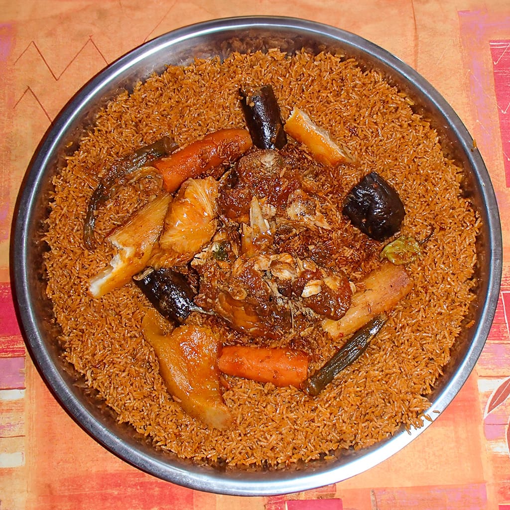 A vibrant plate of Thieboudienne, with spice-infused fish nestled amidst a sea of fiery red rice, dotted with colorful vegetables.